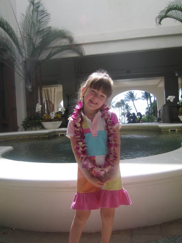 Young girl in dress with pink flowered leis in lobby area of Fairmont Kea Lani in Maui.