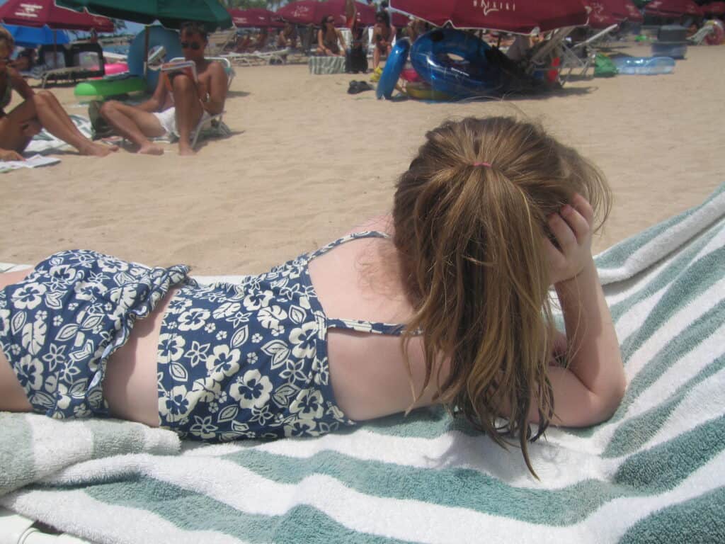 Young girl in blue and white striped bathing suit laying on striped towel on lounge chair on Waikiki Beach's Hilton Hawaiian Village.