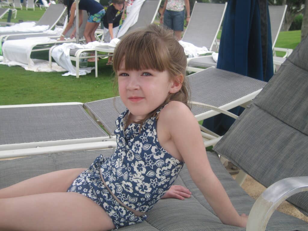 Young girl in dark blue and white flowered bathing suit sitting on pool lounger at Fairmont Kea Lani in Maui.