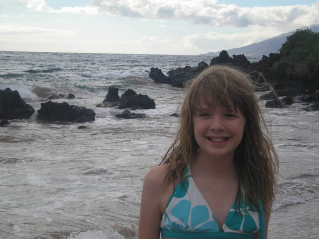 Young girl in blue and white bathing suit top at Fairmont Kea Lani with rocky shore and ocean in background.