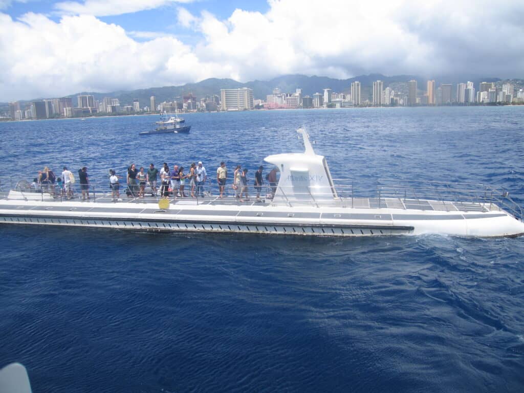 Group of people boarding an Atlantis Submarine with city of Honolulu in background.