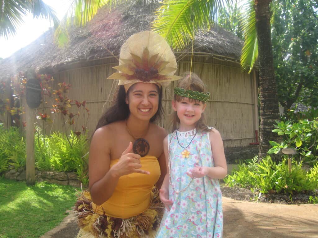 Young girl in blue flowered dress poses with performer at Polynesian Cultural Center on Oahu.