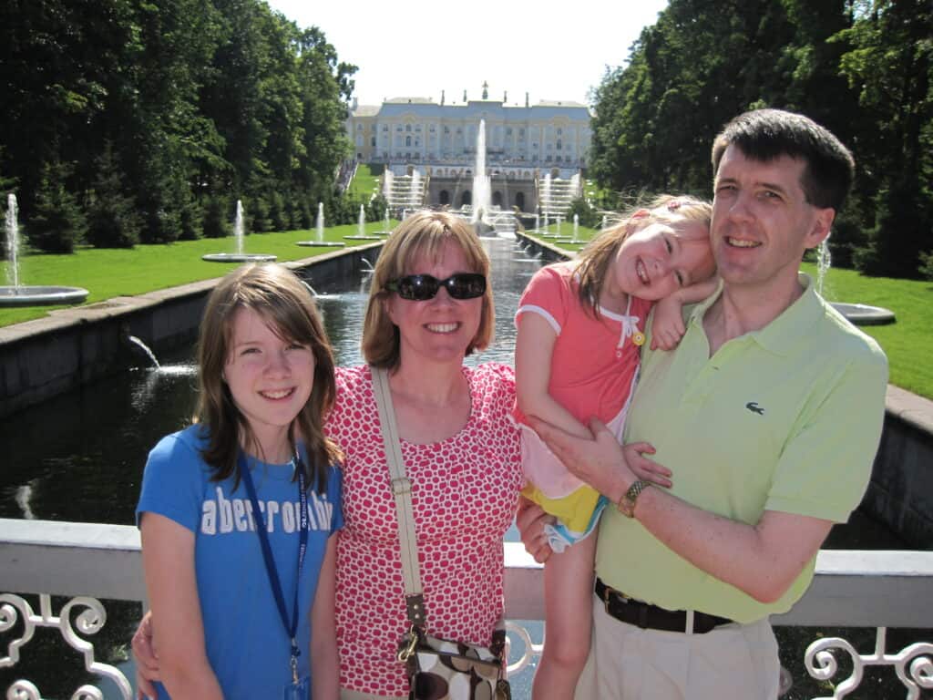 Mom, dad and two daughters in Peterhof Gardens with canal and palace in background.