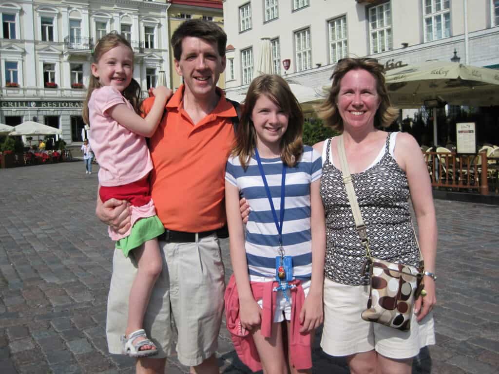 Family in Tallinn's Town Square on summer day - man holding young girl, teen girl and mom.