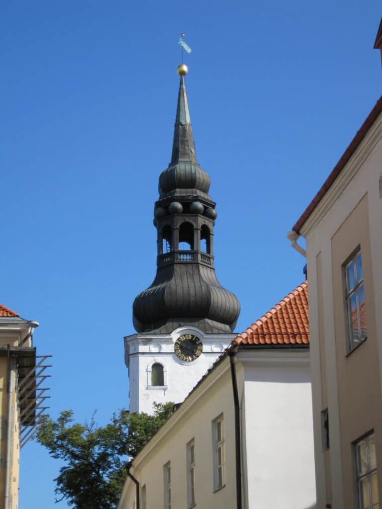 Buildings in Tallinn, Estonia with white building, clock face and black dome/bell tower of St. Mary's Cathedral in background.