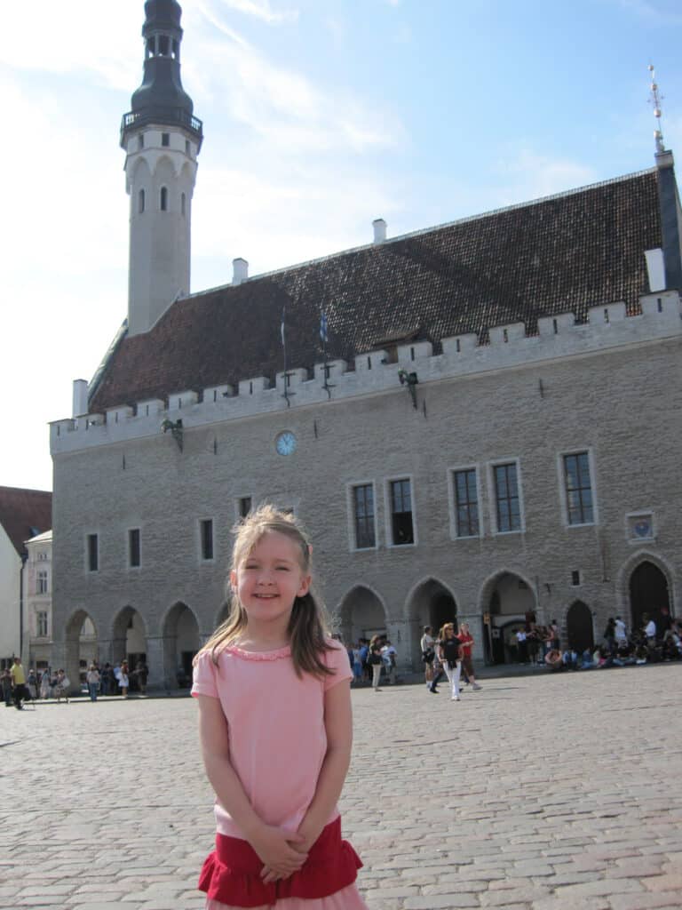 Young girl in pink skirt and t-shirt posing in front of Gothic Town Hall in Tallinn, Estonia.