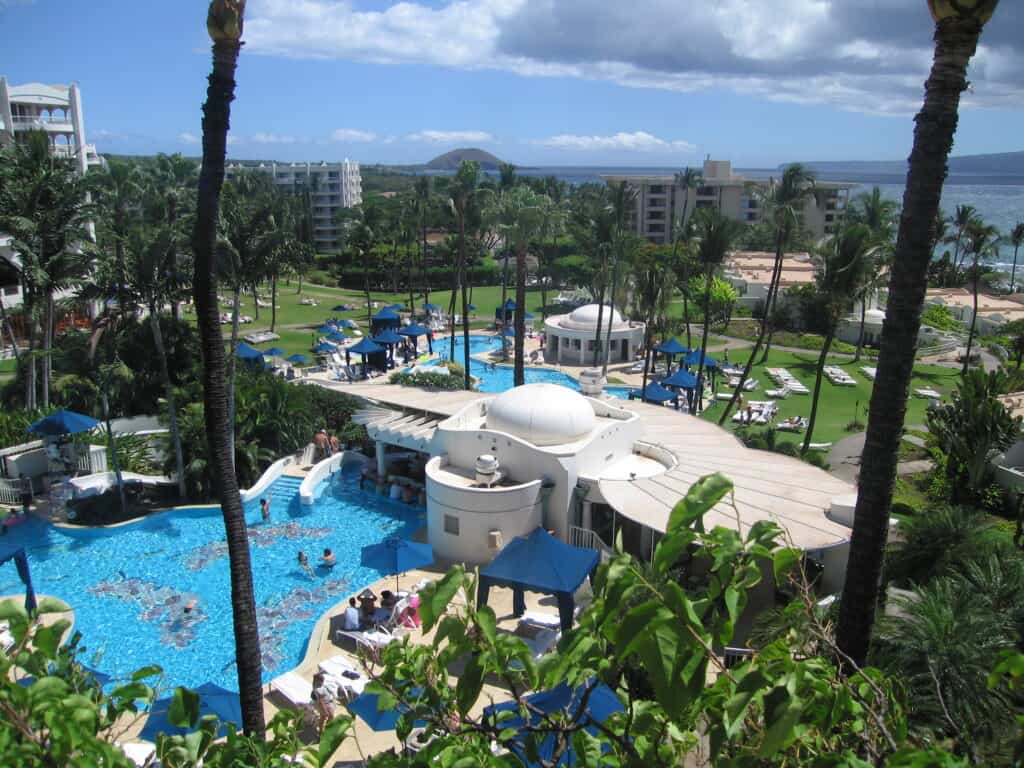 View from a balcony at the Fairmont Kea Lani, Maui - pools, white buildings, palm trees, buildings and ocean in background.