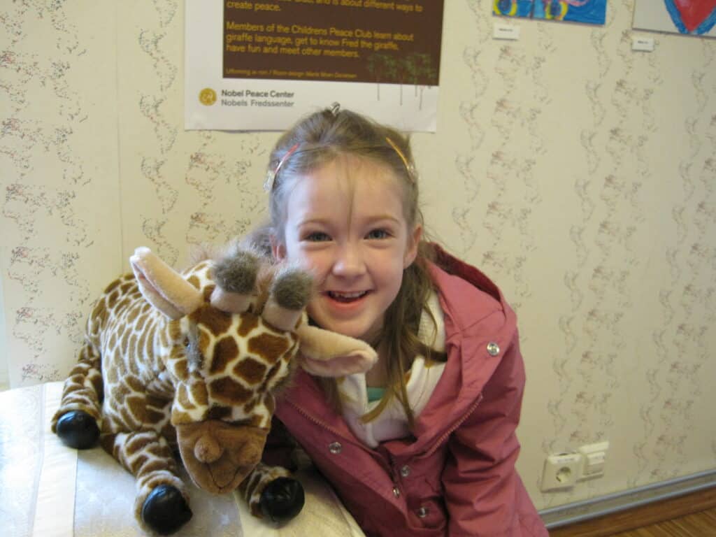 Young girl in pink jacket with small stuffed giraffe in children's activity area at Nobel Peace Center in Oslo, Norway.