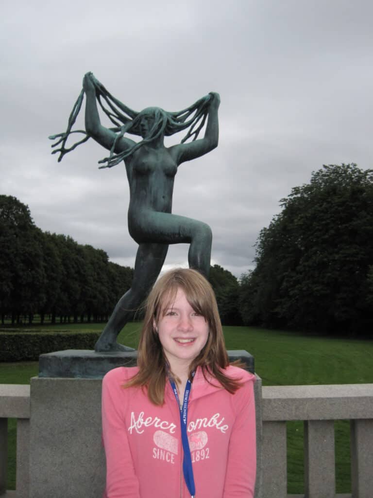 Teen Girl in pink hoodie in front of sculpture in Vigeland Park, Oslo.