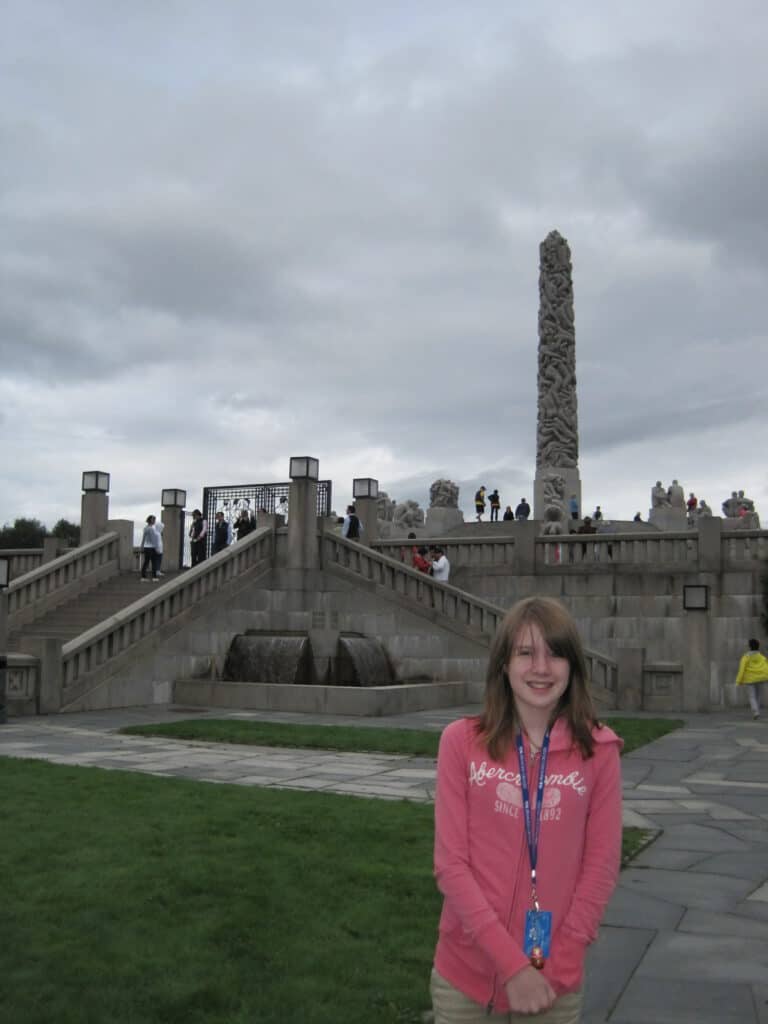 Young teen girl in pink hoodie at Vigeland Park, Oslo with The Monolith in background.