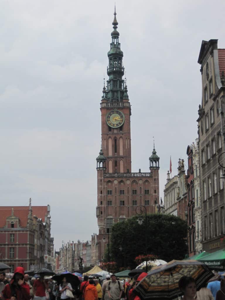 Gdansk Town Hall on rainy day with crowd of people carrying umbrellas.