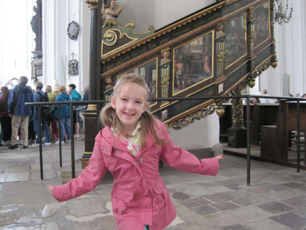 Young girl in pink coat with tour group in background inside St. Mary's church, Gdansk, Poland.