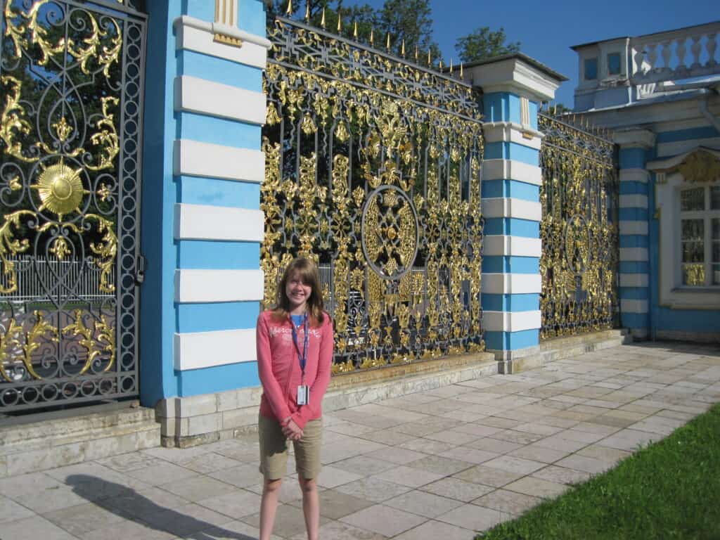 Young girl in shorts and pink sweatshirt standing in front of gates to Catherine's Palace in St. Petersburg, Russia.