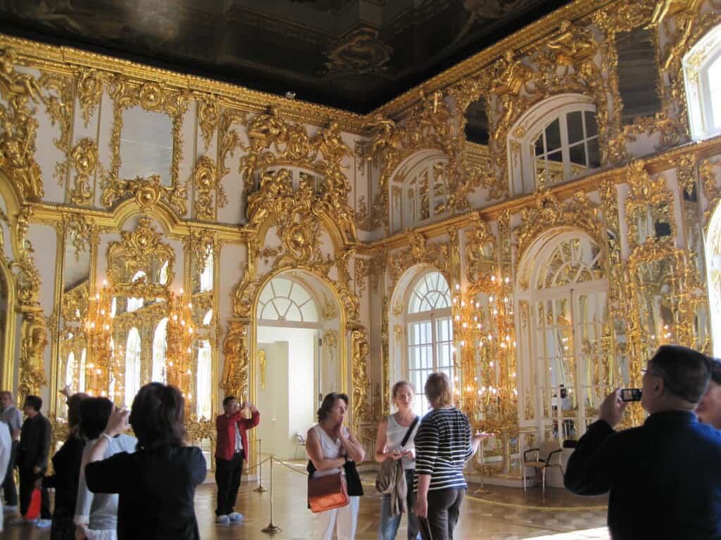 People talking and taking photos in the lavish gold-decorated Great Hall at Catherine's Palace, Russia.