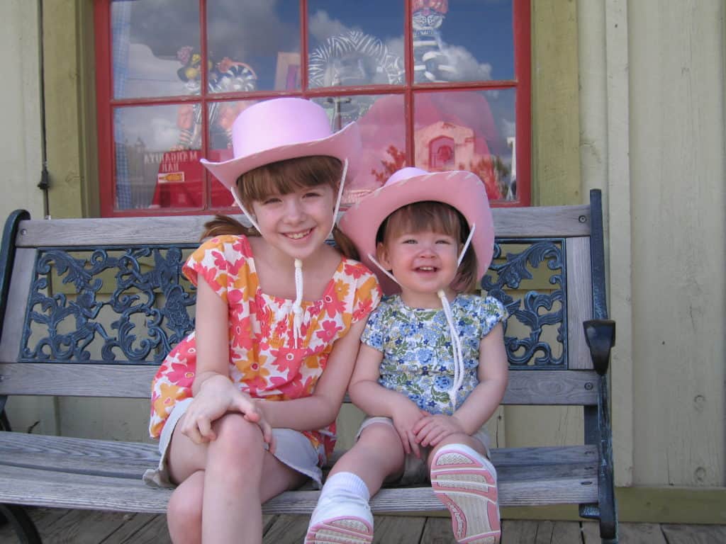 Two young girls in pink cowboy hats sitting on a bench at Rawhide, Scottsdale, Arizona.