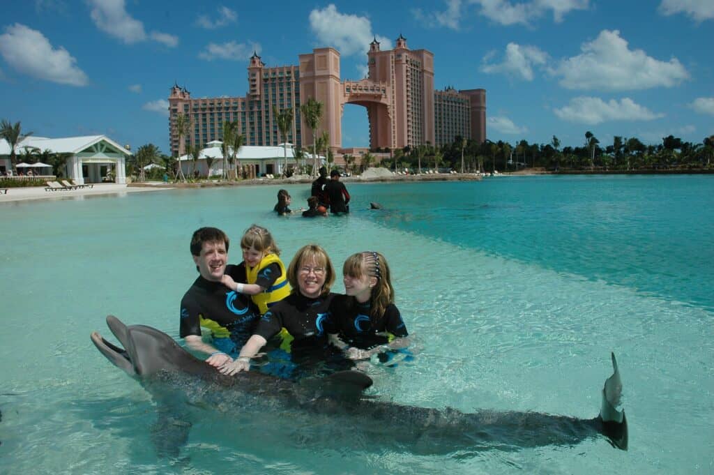 Family of mom, dad and two daughters posing with dolphin at Dolphin Cay, Atlantis Bahamas.