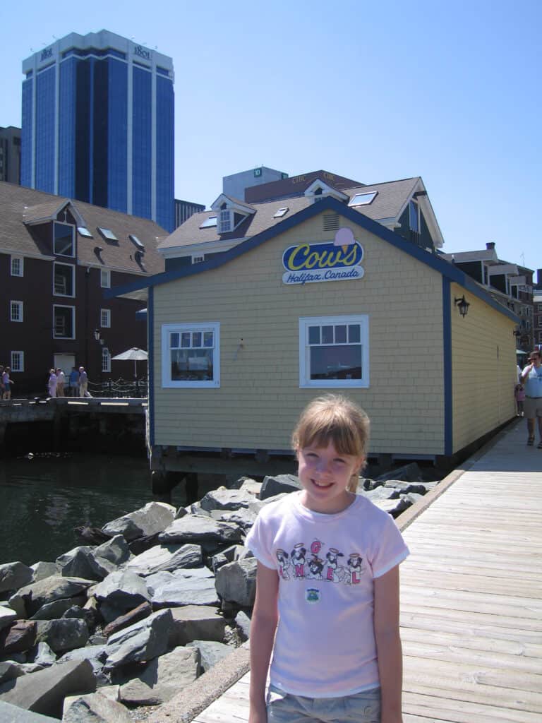 Young girl poses on boardwalk in Halifax with Cows Ice Cream shop in background.