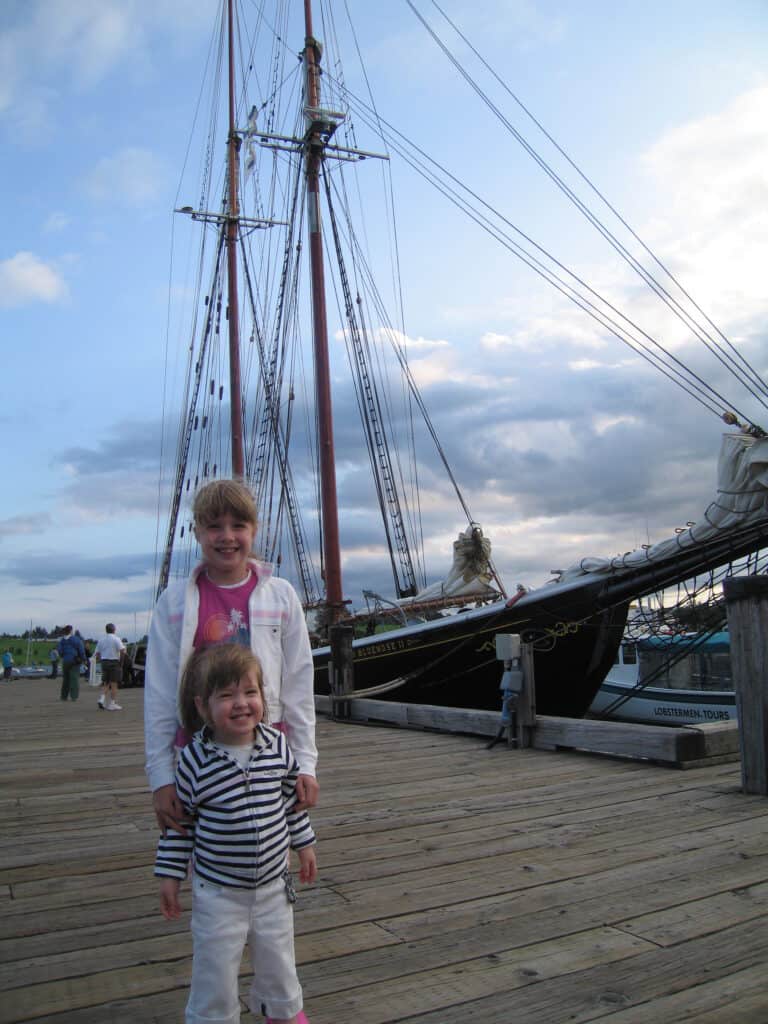 Two young girls posing in front of Bluenose II schooner docked in Lunenburg, Nova Scotia.