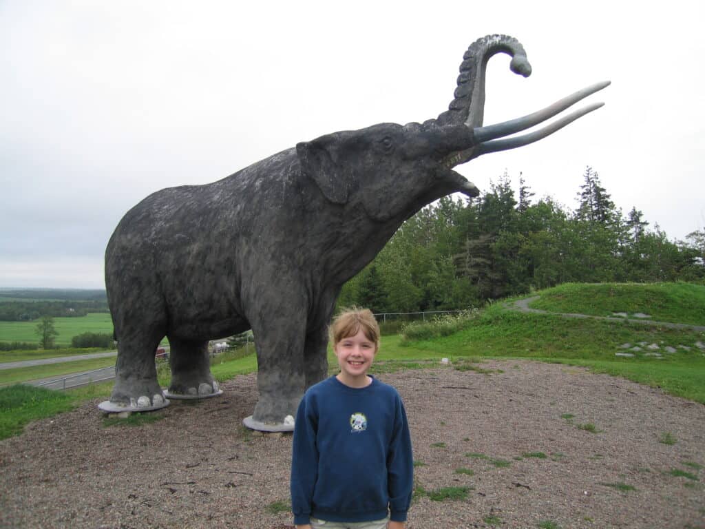 Young girl in navy blue sweatshirt standing in front of "mastodon" at rest stop in Stewiacke, Nova Scotia.