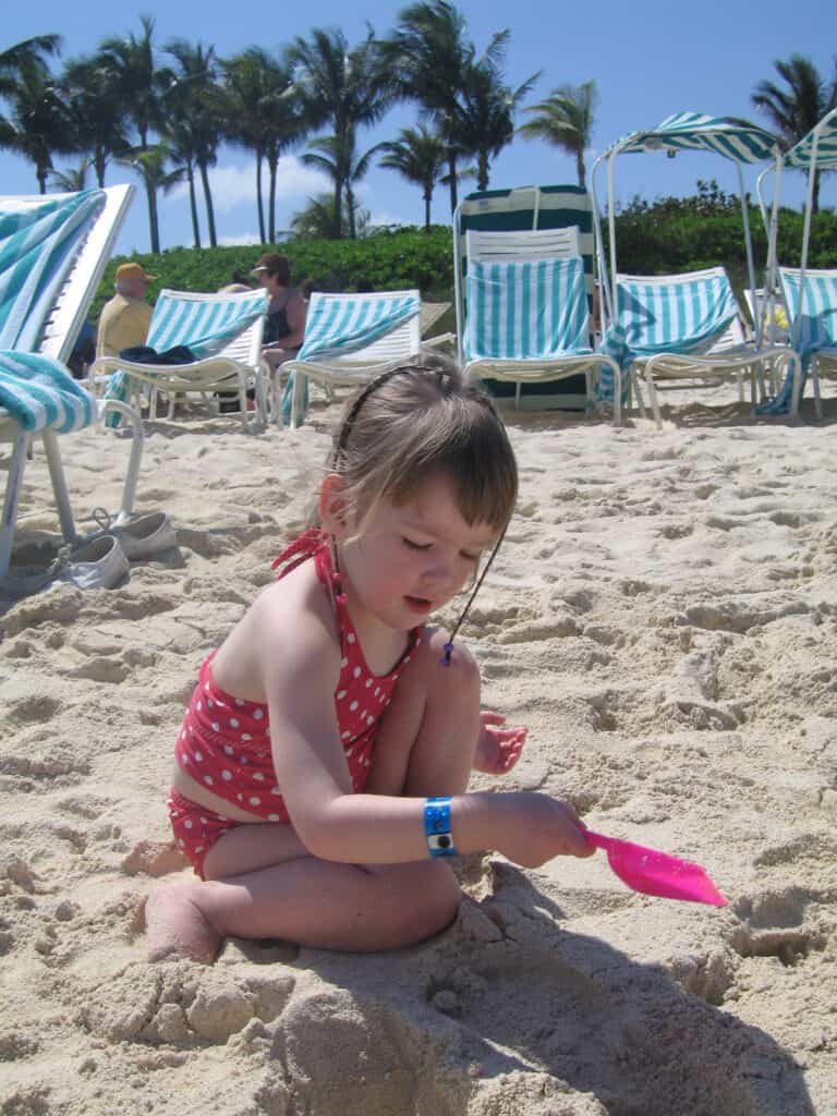 Young girl in red and white polka dot swimsuit playing in sand on beach at Atlantis Bahamas.