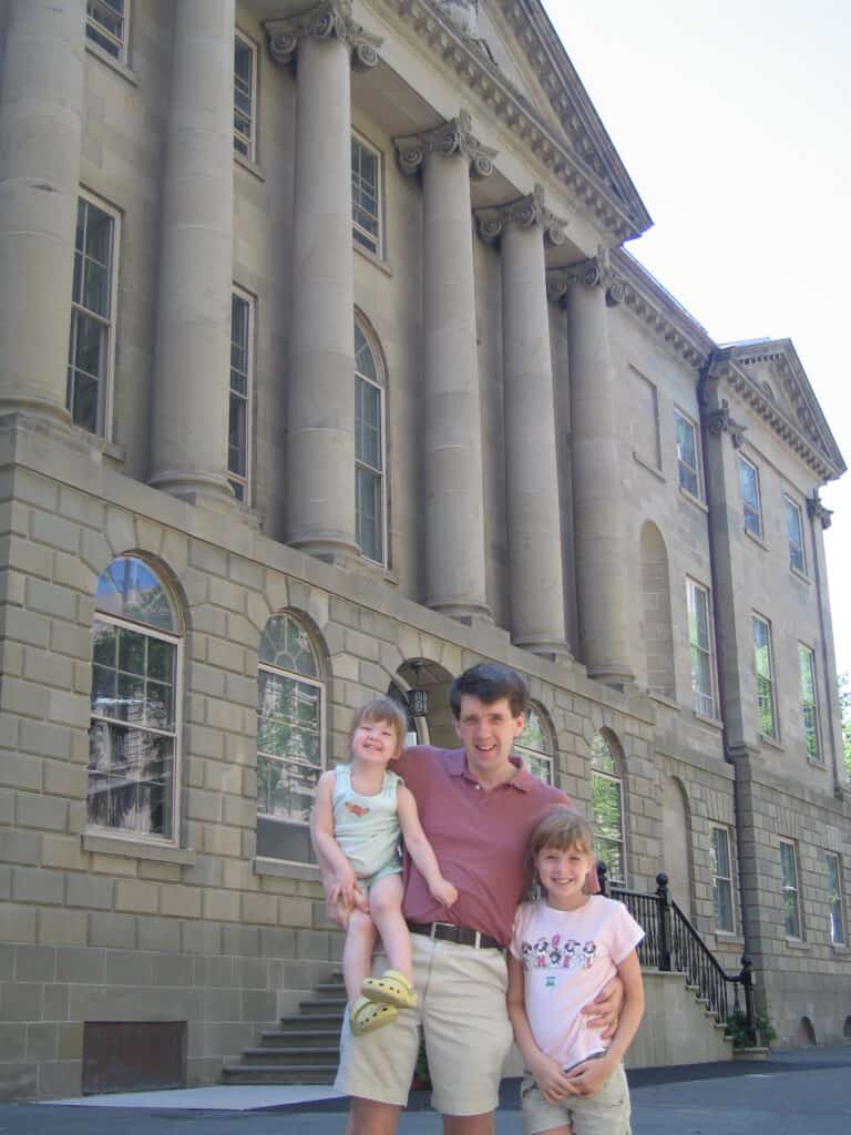 Man standing beside one daughter while holding younger girl outside Province House, Halifax, Nova Scotia.