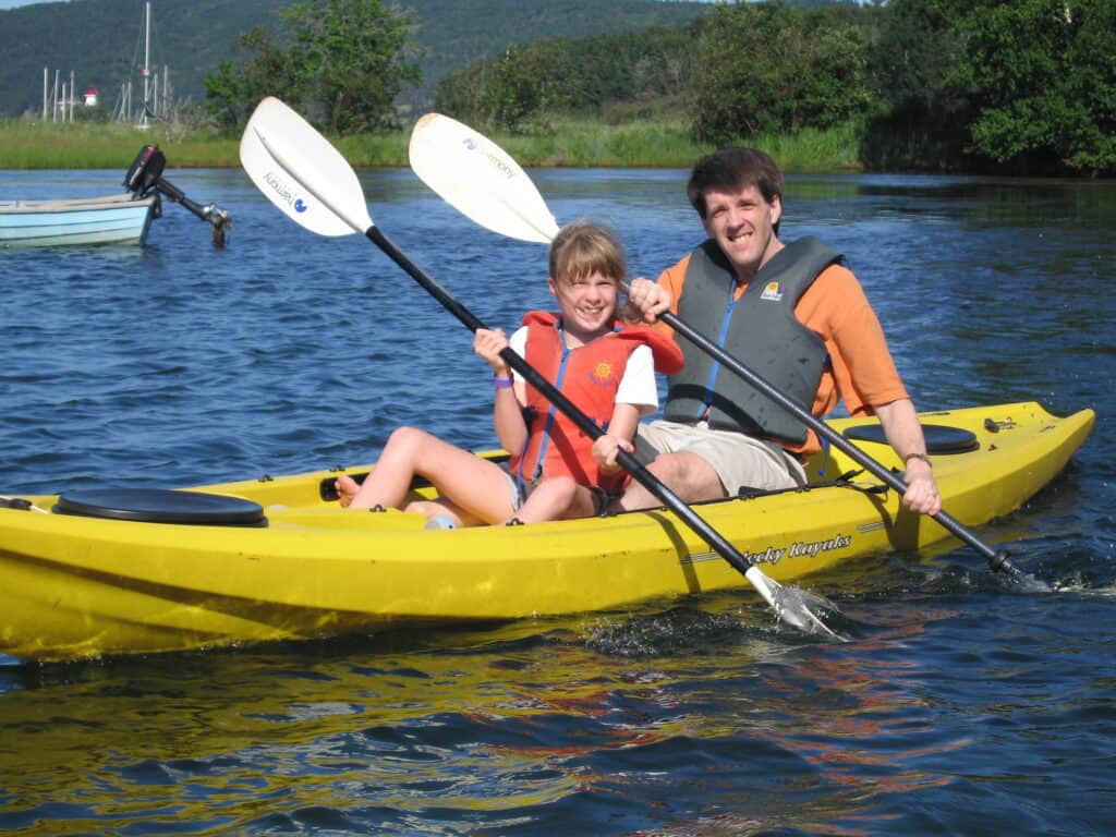 Dad and daughter wearing life jackets in yellow kayak on lake at Inverary Resort in Baddeck on Cape Breton Island in Nova Scotia.