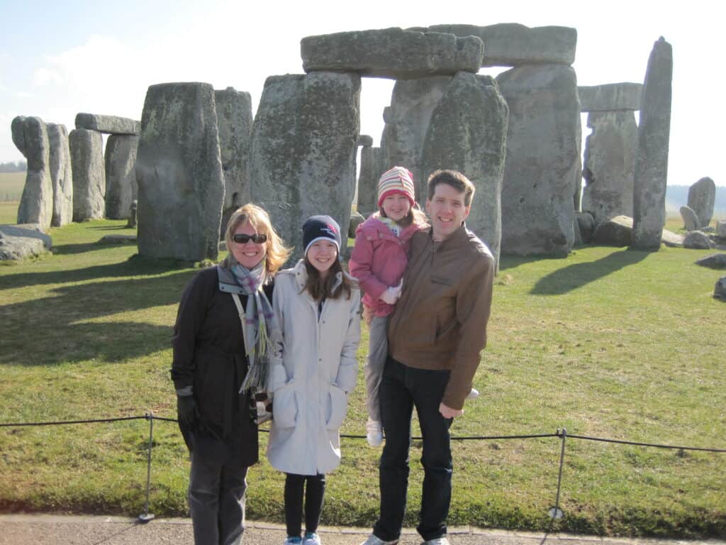 Family of four at Stonehenge - mom, teen girl and dad holding younger girl.