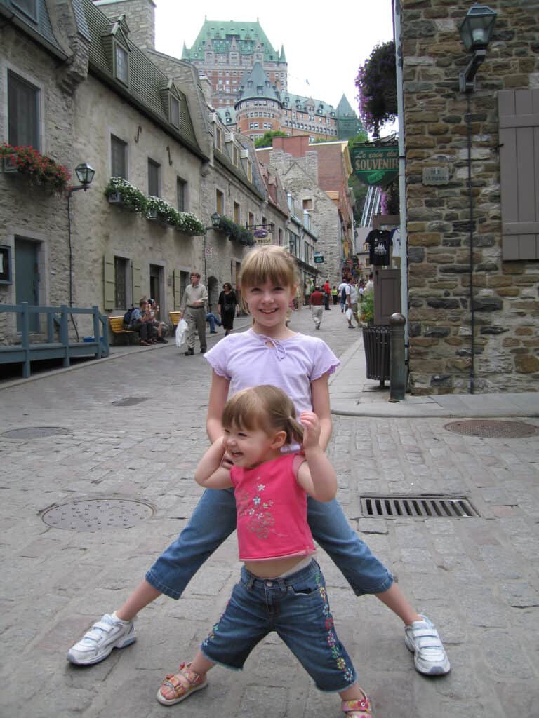 Two young girls posing in lower town of quebec city with chateau frontenac in background.