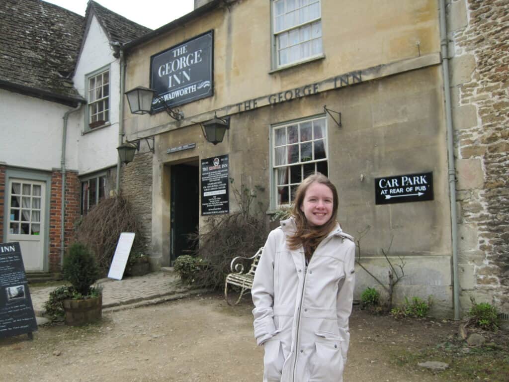 young girl in light coloured coat standing outside the george inn, Lacock, England.