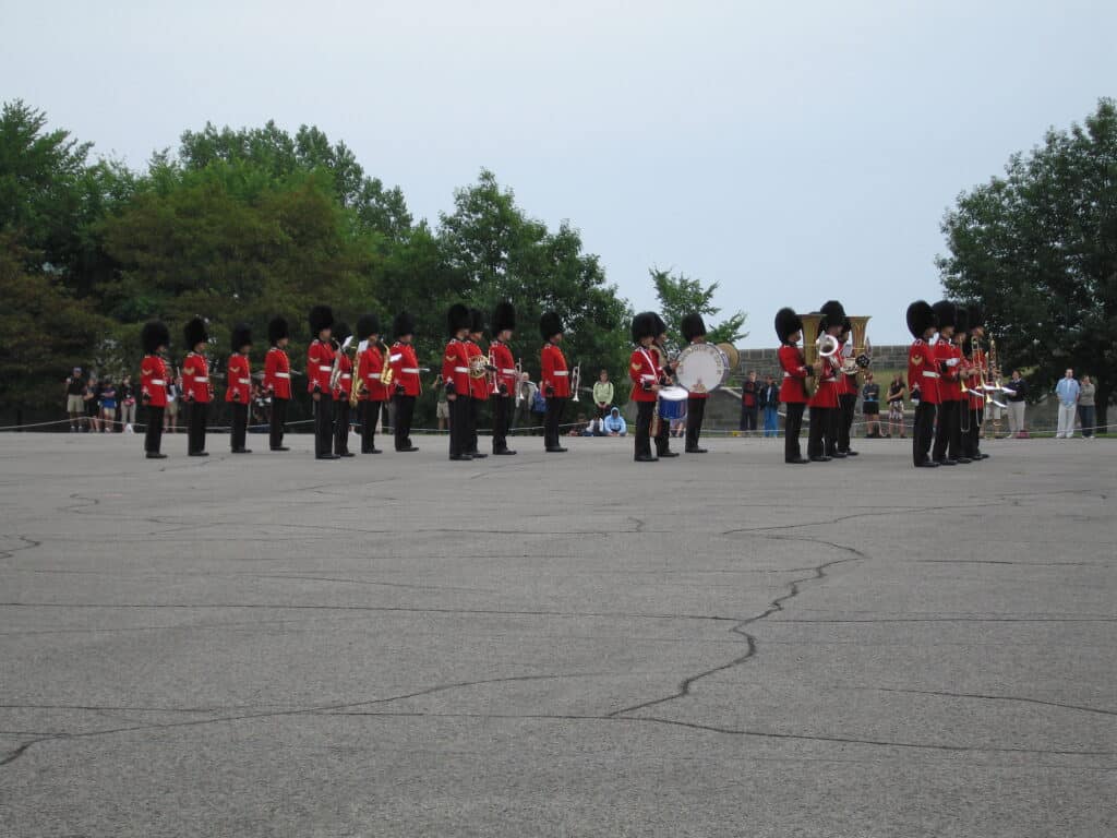 Soldiers in black pants, red jackets and black fur hats holding instruments lined up for the Changing of the Guard at La Citadelle in Quebec City, Canada.