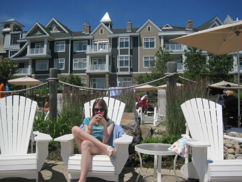 Teen girl sitting in white adirondack chair using cellphone with resort in background.