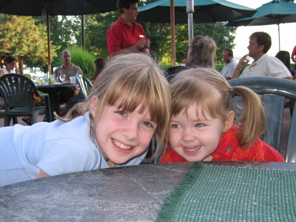 two smiling young girls sitting with heads close together at table on outdoor patio at fairmont chateau montebello in quebec.