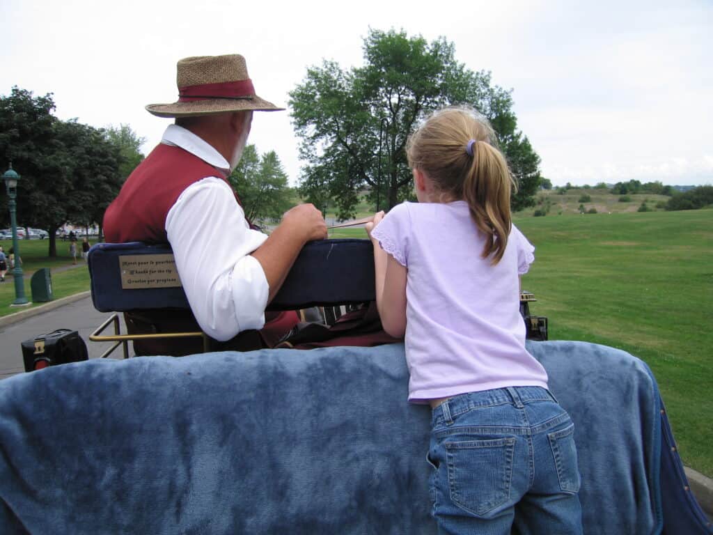 Driver of carriage helping young girl holding reins.