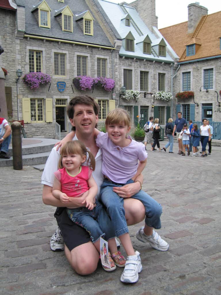 Dad kneeling with two young daughters in Place Royale, Quebec City.