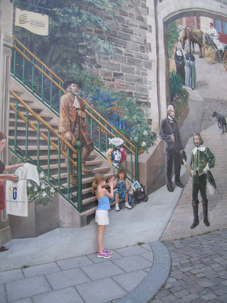 Young girl in white shorts and blue tank top posing with the fresque de quebecois wall mural in quebec city's lower town.