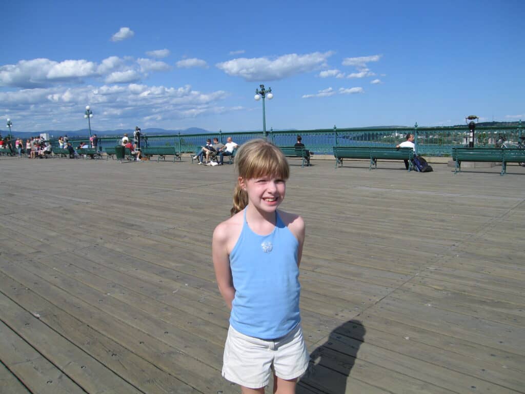 Young girl in white shorts and blue tank top on boardwalk by chateau frontenac in quebec city with st. lawrence river in background.