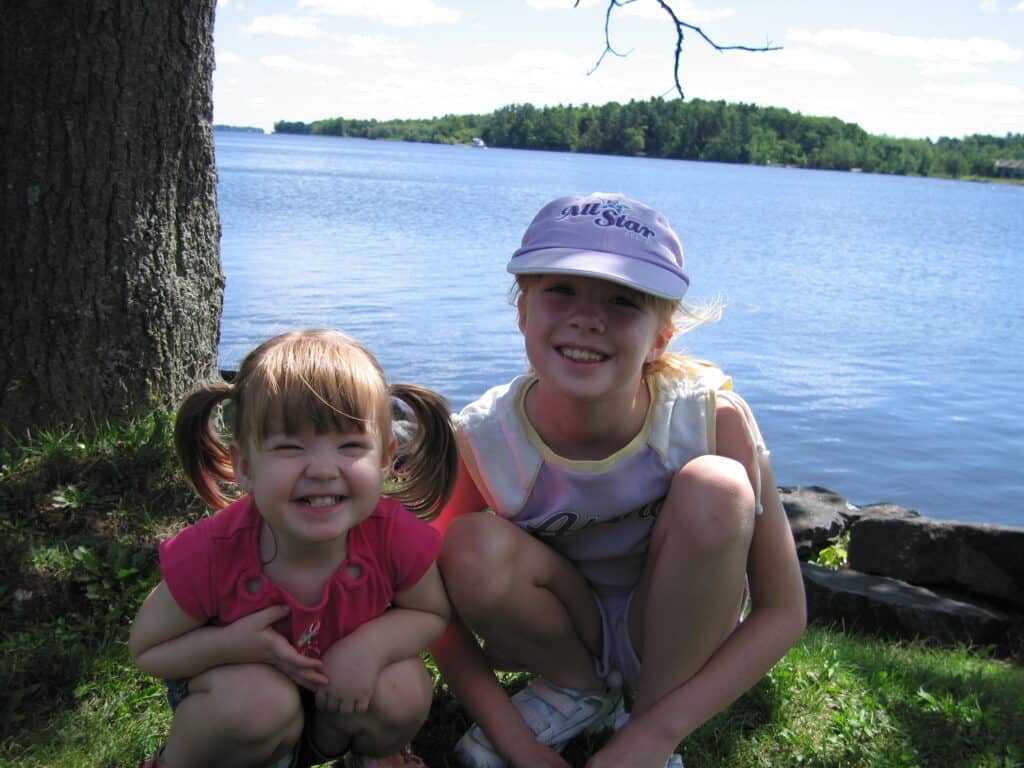 two young girls sitting on ground with outaouis river in background at chateau montebello.