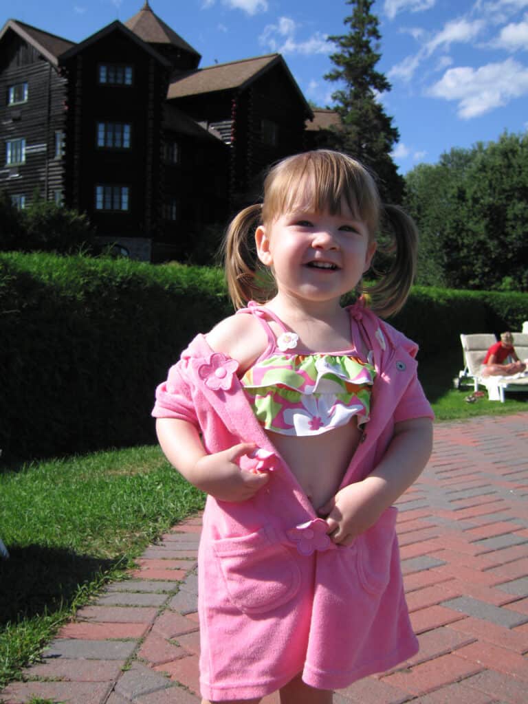 toddler girl in pink and green flowered bathing suit and pink robe by outdoor pool at chateau montebello with resort in background.