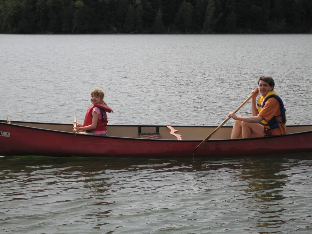 Young girl and dad wearing lifejackets and holding paddles in canoe on Whitefish Lake, Montebello.