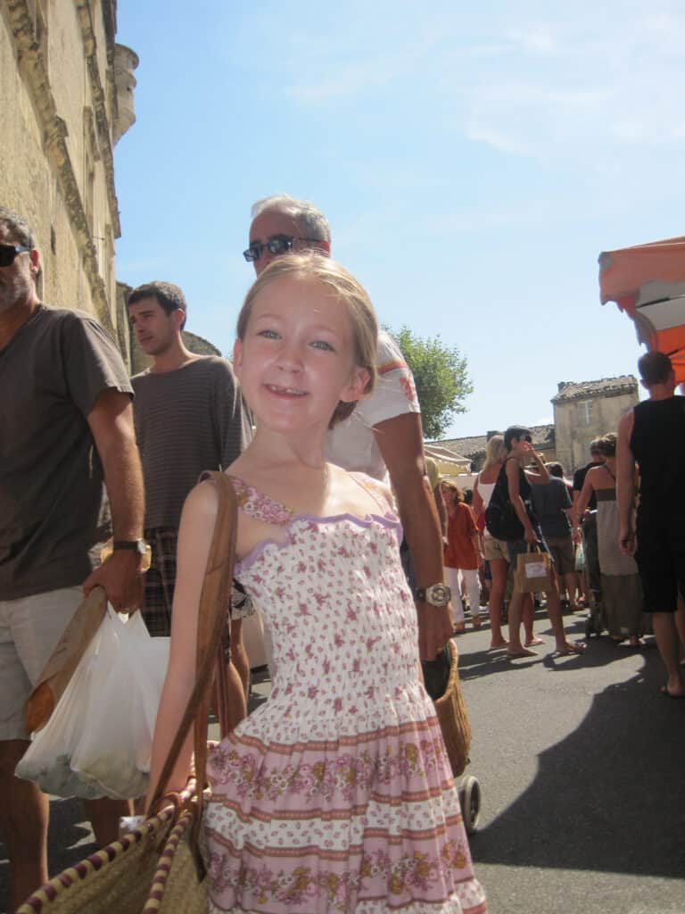 young girl in dress holding straw basket at the market in gordes.