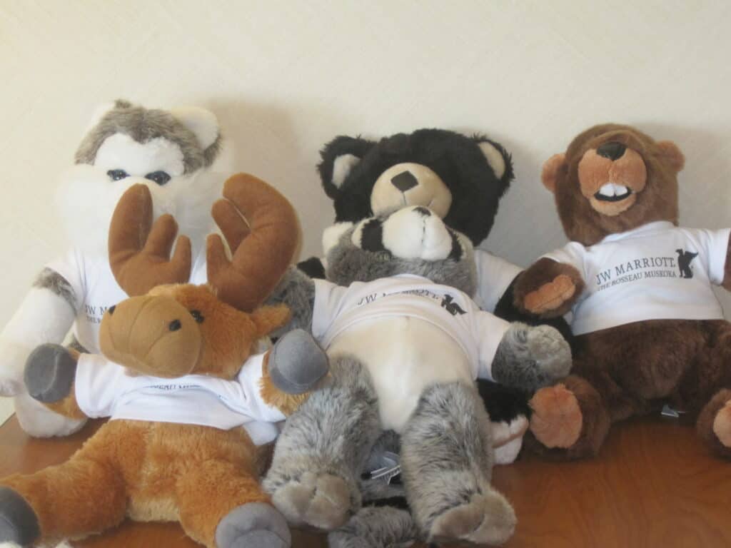 five stuffed animals wearing JW Marriott The Rosseau Muskoka t-shirts - a wolf, a bear and a beaver in back row and a moose and a racoon in front.