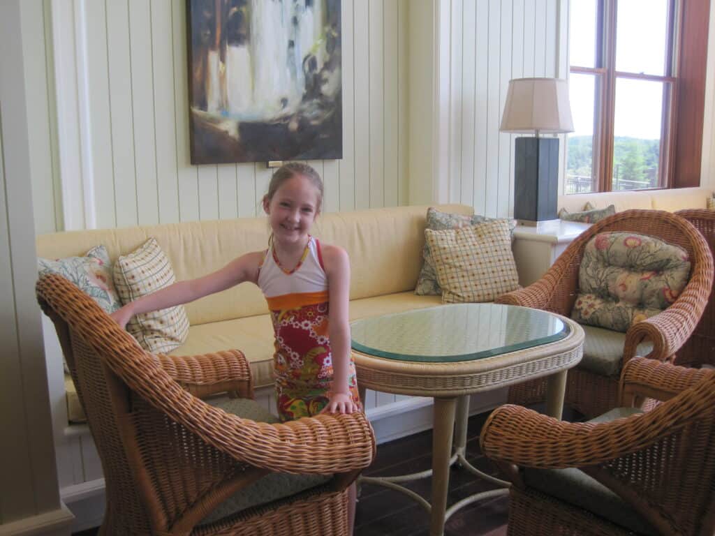 young girl in muskoka room at the rosseau muskoka - white panelled wall in seating area with upholstered and wicker furniture with throw cushions.