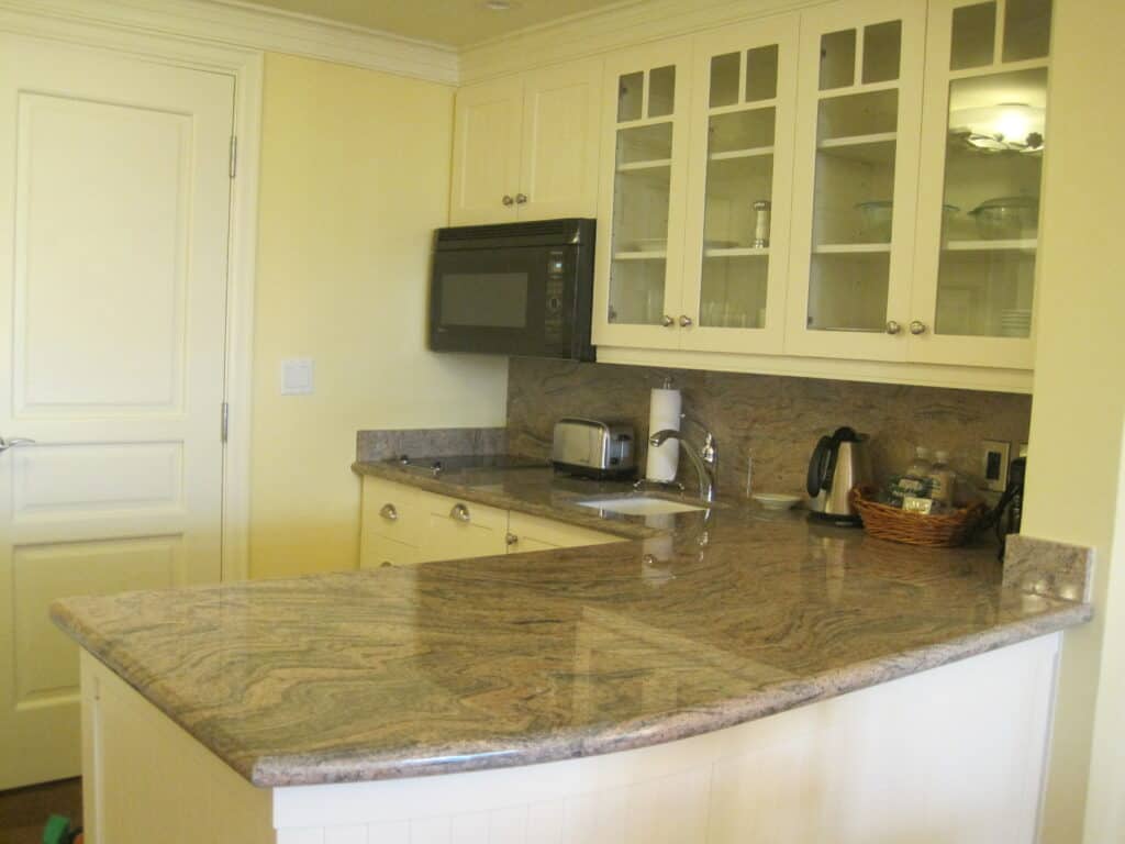 L-shaped kitchen area with upper cabinets with glass doors in one bedroom suite at rosseau muskoka - under cabinet black microwave, toaster, kettle, paper towel holder and basket of supplies on counter.