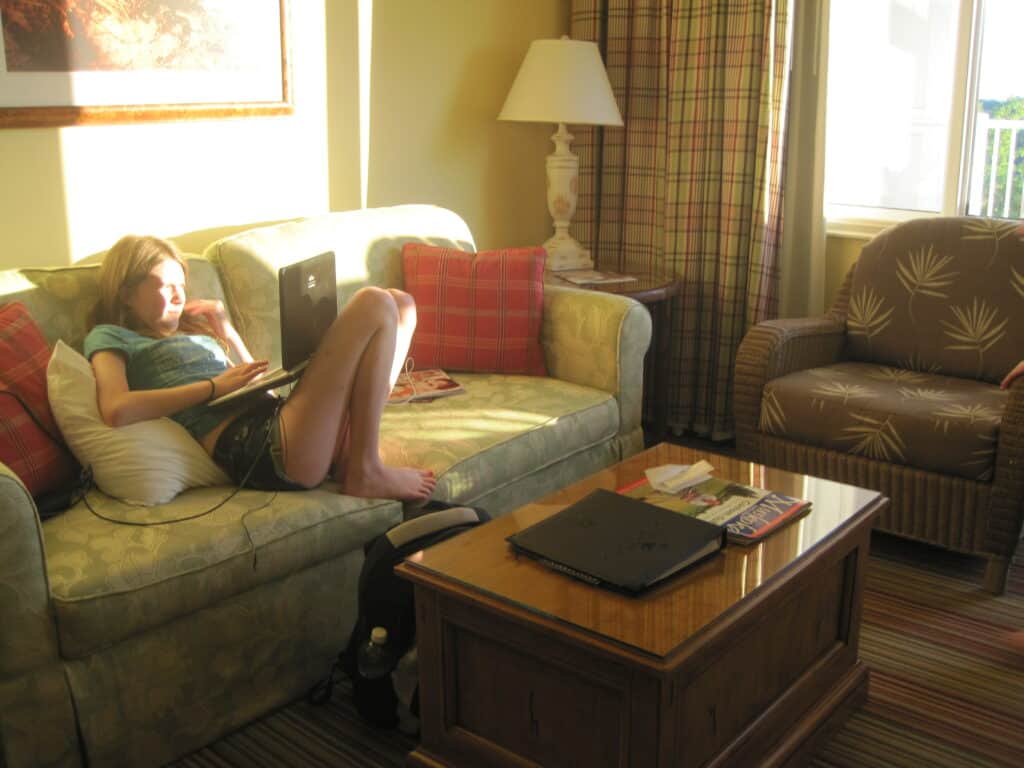 Rosseau Muskoka - teen girl in shorts and t-shirt on sofa in seating area of one bedroom suite with sun shining in window.