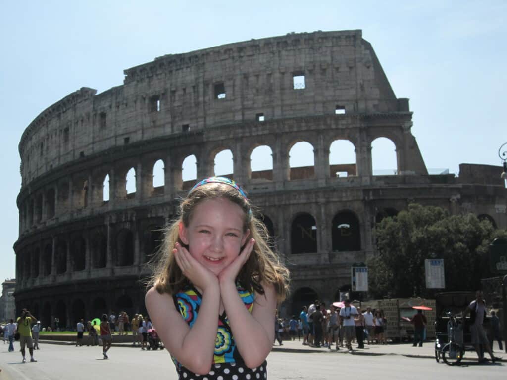 young girl in dressing holding hands to face with Colosseum in background.