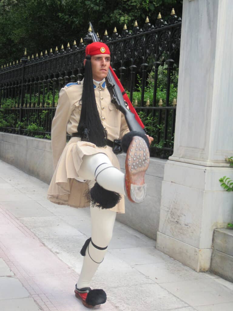 Changing of the Guard ceremony in Athens with one of the Evzones in front of fence with leg kicked up in front.