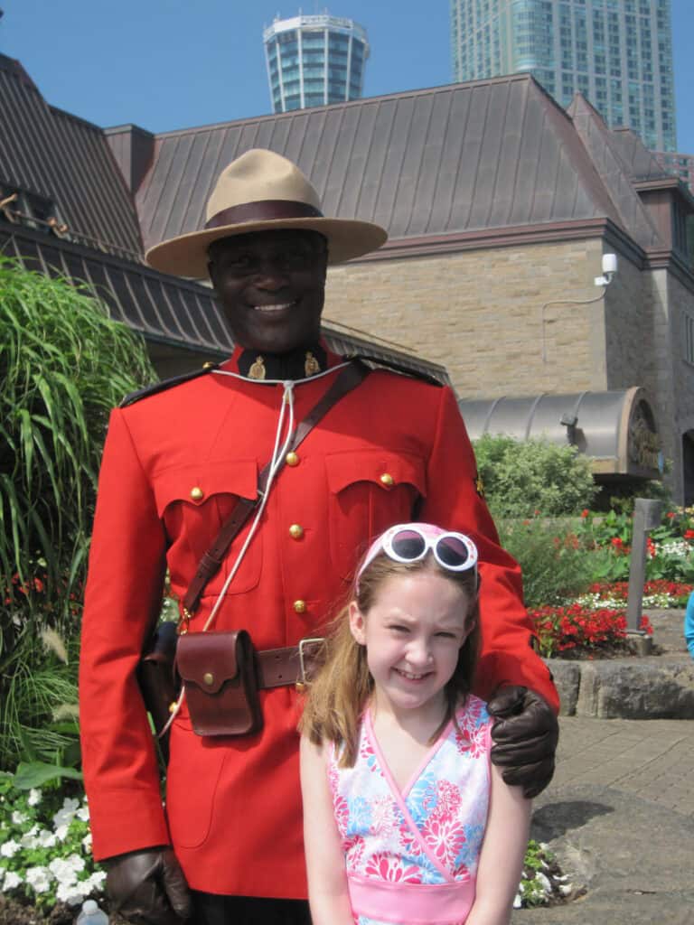 Young girl in dress with round white  sunglasses on top of head poses with Mountie.