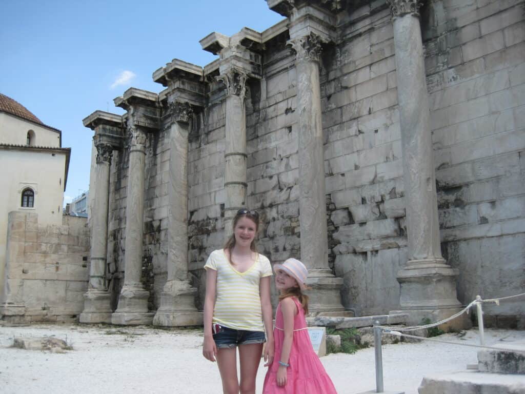 Teen girl and younger girl standing outside roped off area with ancient building and columns in background in Ancient Agora area of Athens, Greece.