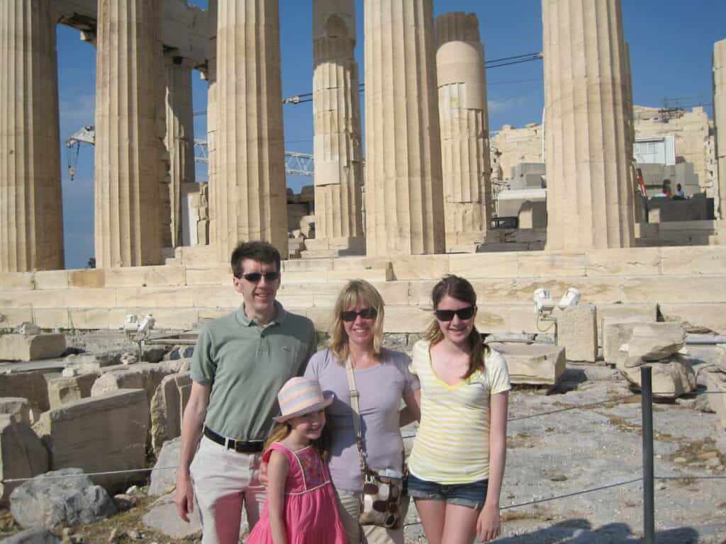 Family of four - dad, mom, teenage girl and younger girl standing in front of the Parthenon in Athens.