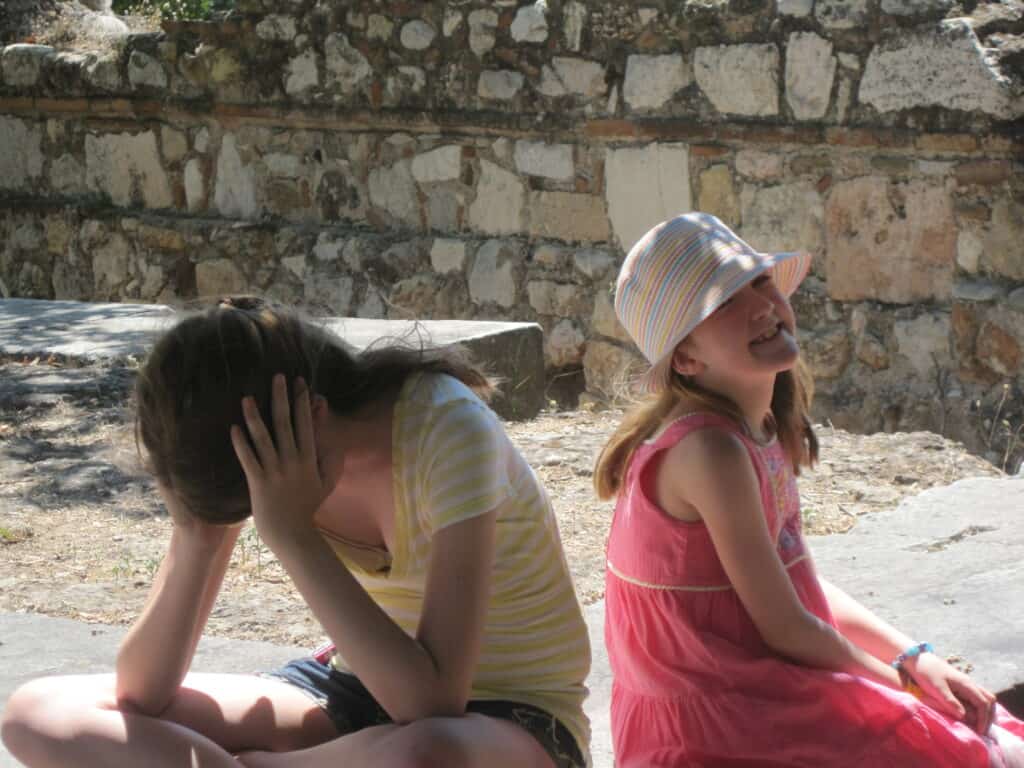 Teen girl holding head in hands and younger girl looking exhausted sitting on a bench in Athens.